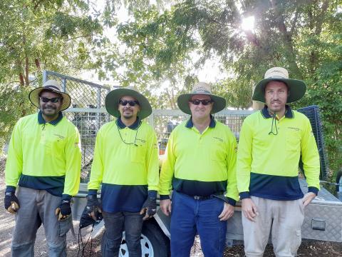 A group of four people stood in front of a ute, wearing yellow hi vis shirts. They're all smiling at the camera.